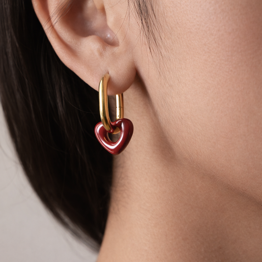 Gold hoop earring with a red heart charm worn by a person.