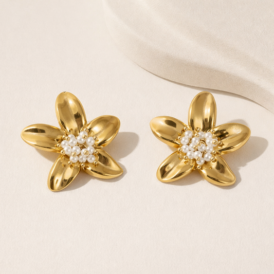 Pair of gold flower-shaped earrings with pearl centers on a beige background